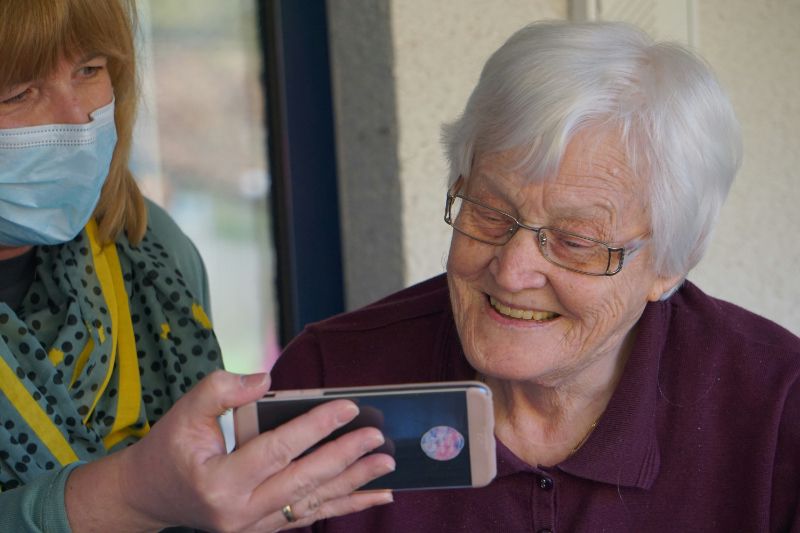 Elderly woman and  caregiver looking at their phones in nursing home